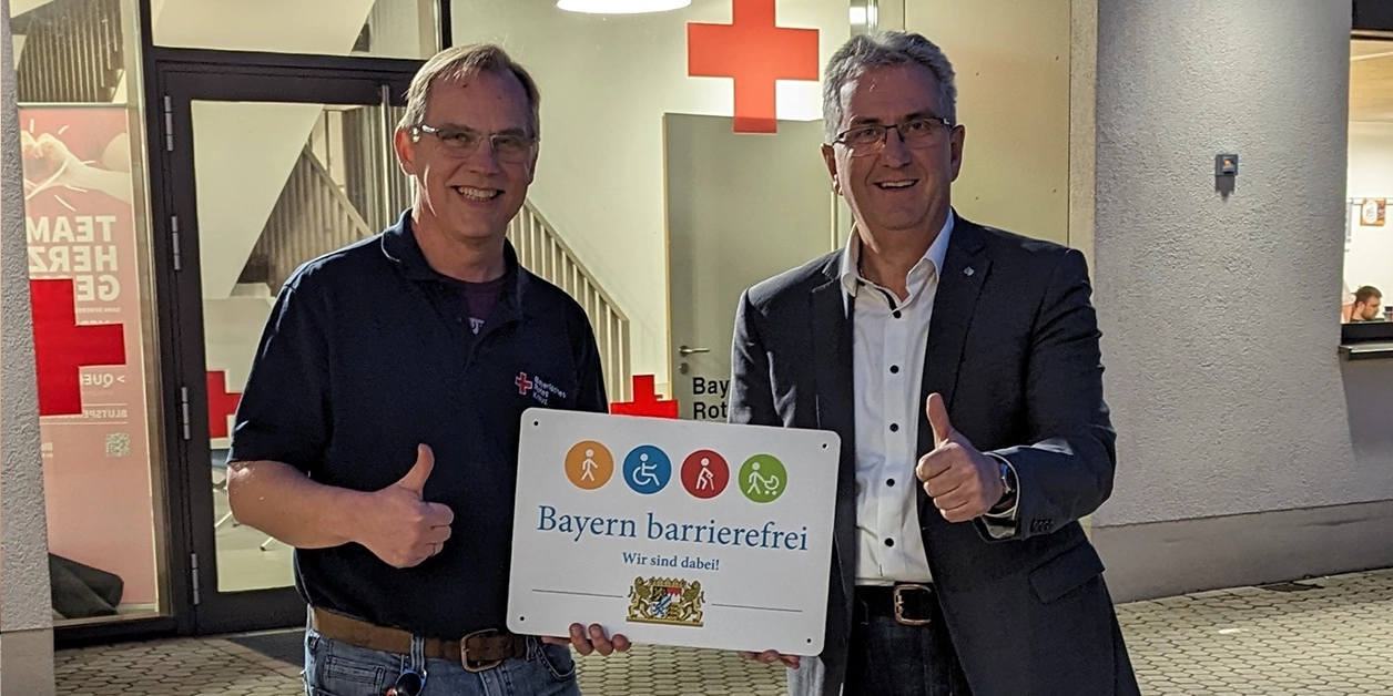 Präsentation des Signets „Bayern barrierefrei“ vor der BRK Unterkunft Stein.