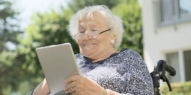 Eine ältere Frau blickt auf ein Tablet.