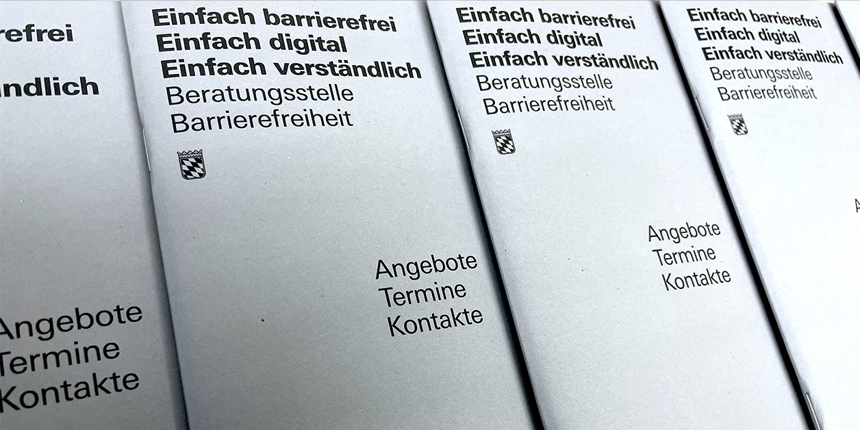 Mehrere hellgraue Broschüren der Beratungsstelle Barrierefreiheit liegen aufgefächert nebeneinander. 