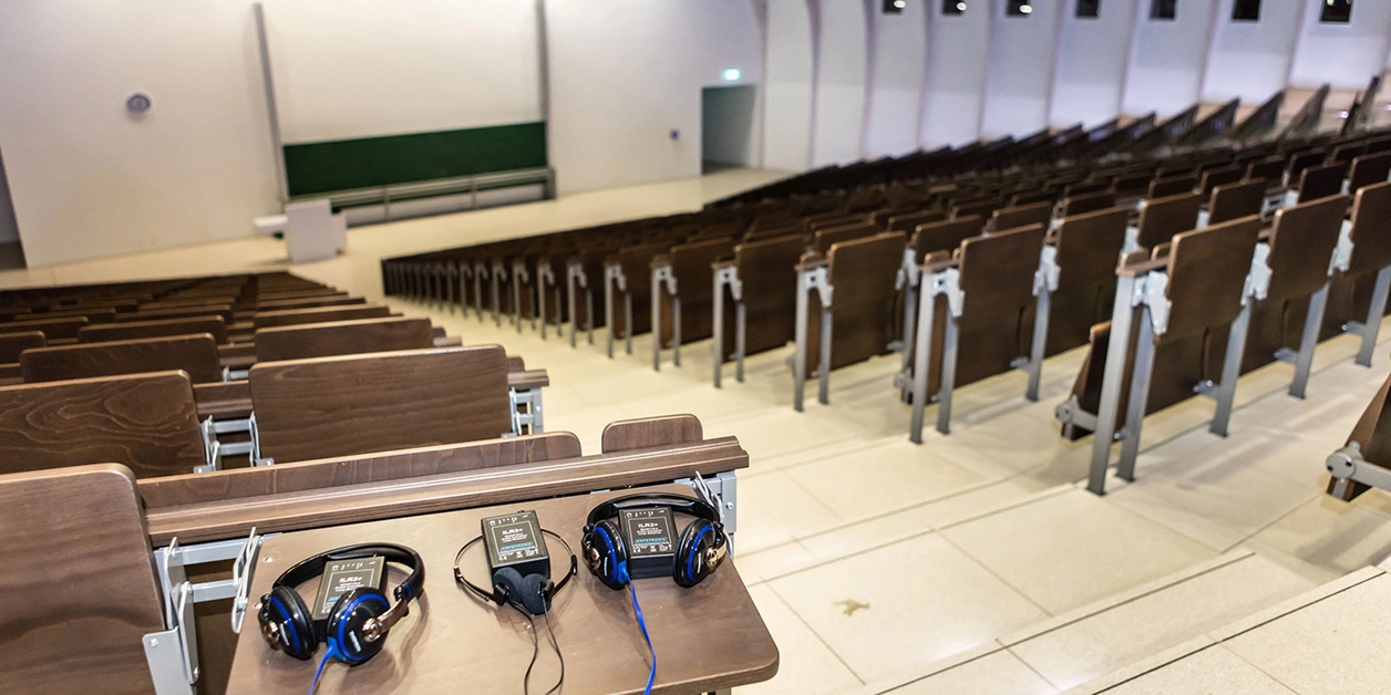 Großer Hörsaal; im Vordergrund Ablage mit Audio-Empfangsgeräten.