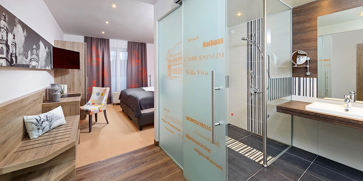 Blick in ein Hotelzimmer, rechts ein Badezimmer mit offener Schiebetür und bodenebener Dusche.