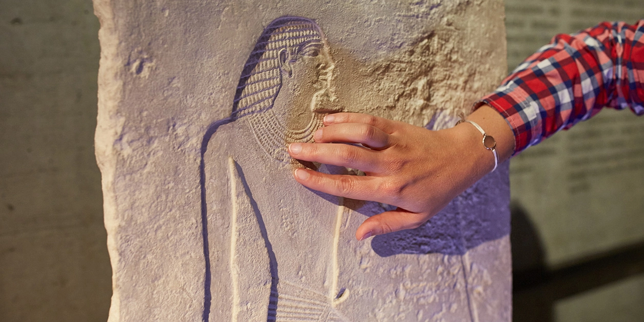 Hand einer Besucherin ertastet eine Relieffigur im Museum.