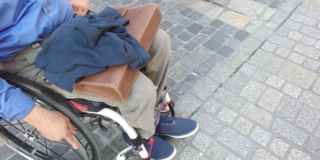 Ein Mann steht mit seinem Rollstuhl in einer Fußgängerzone, am Übergang von grober zu abgeflachter, rollstuhlfreundlicher Pflasterung.