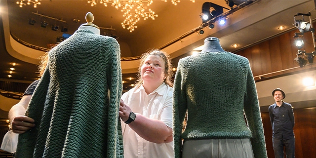 Auf einer Theaterbühne: Eine Frau ertastet ein Kostüm auf einer Schneiderpuppe.