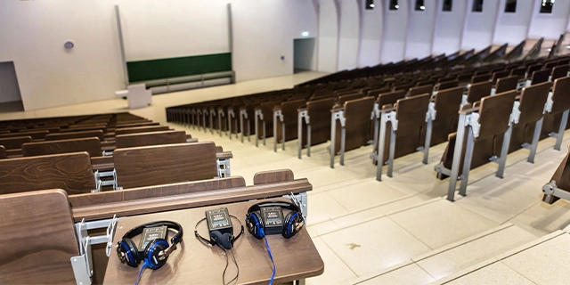 Großer Hörsaal; im Vordergrund Ablage mit Audio-Empfangsgeräten.