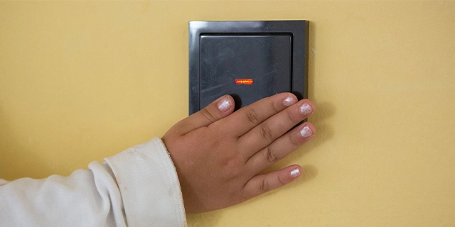 Nahaufnahme: Ein kleines Mädchen drückt auf einen Lichtschalter. Der dunkle Schalter hebt sich deutlich von der hellgelben Wand ab.