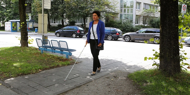 Irmgard Badura ist mit dem Langstock unterwegs an der Münchner Bushaltestelle Infanteriestraße.