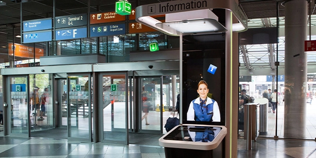 Blick in ein Flughafengebäude; im Vordergrund ein interaktives Info-Terminal.