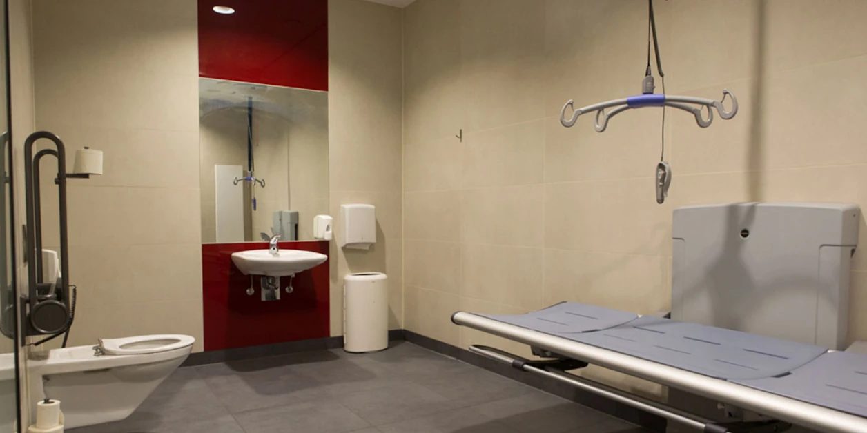 Innenraum einer Behindertentoilette mit Lifter und Liege.