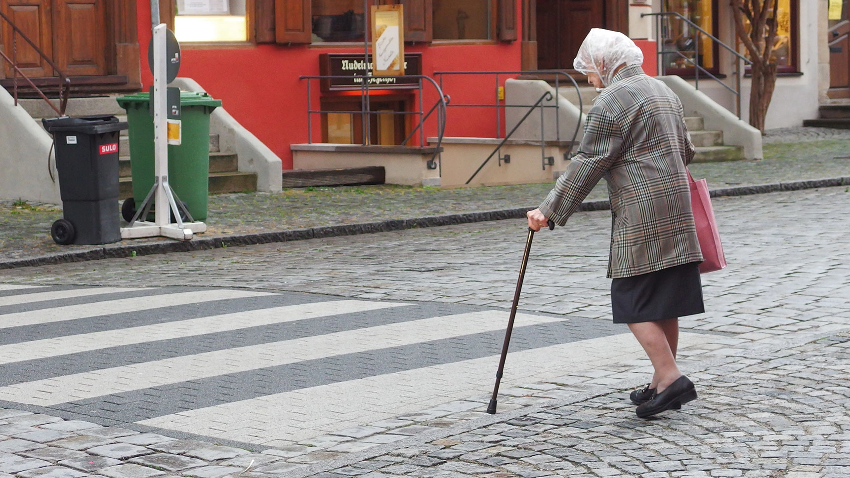Ältere Frau mit Gehstock überquert Zebrastreifen.