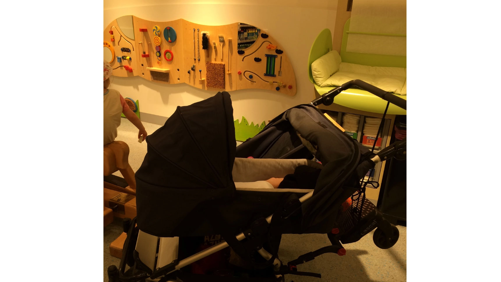  Ein Kinderwagen steht vor einer Spielecke mit Wickeltisch.