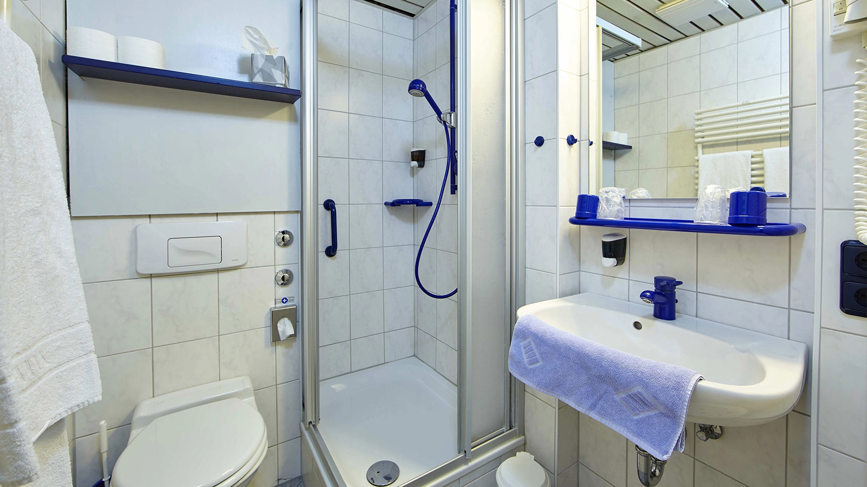 Badezimmer, in dem sich Armaturen und Ablagen in kräftigen Farben von den Fliesen abheben.