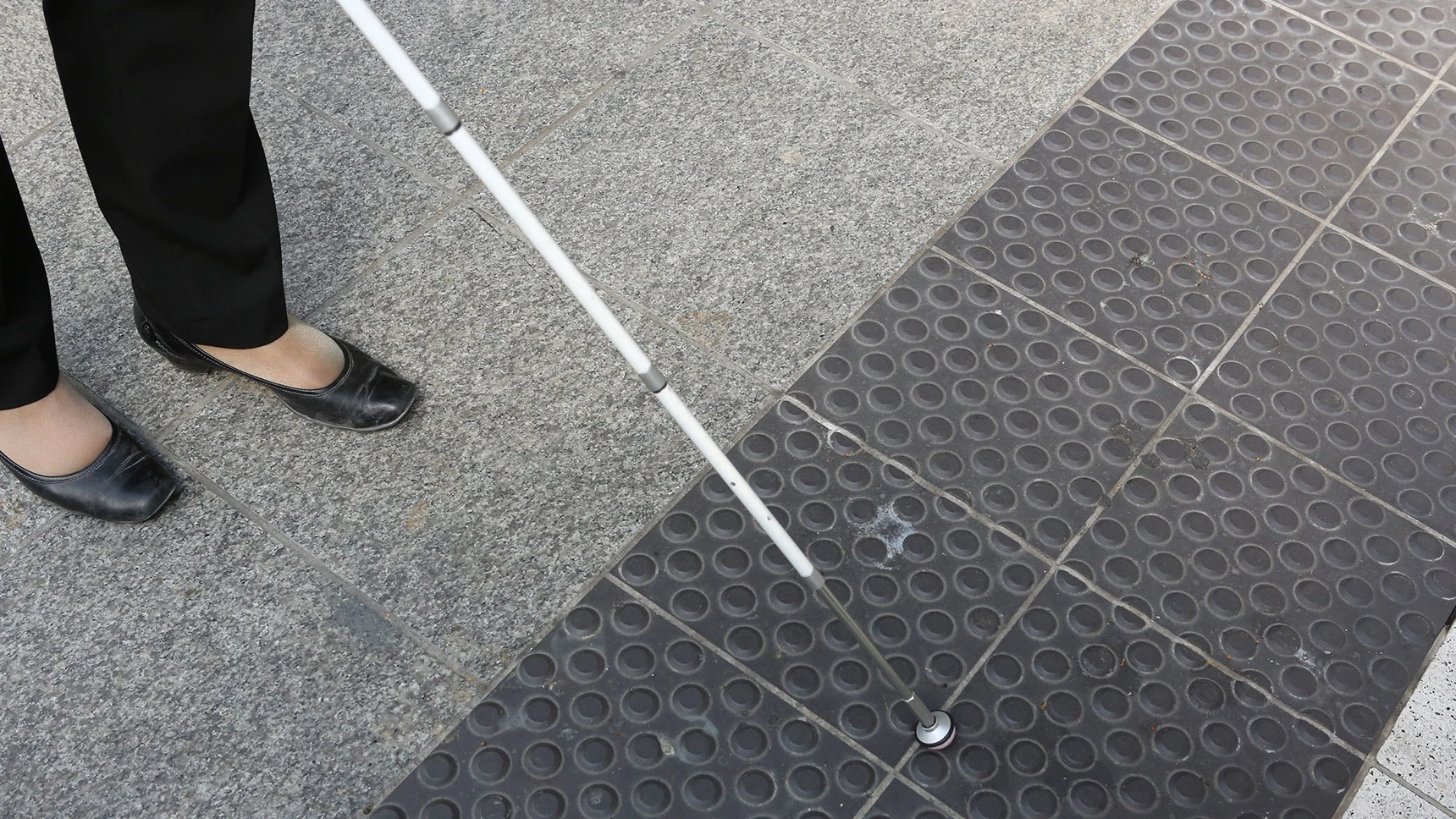 Ein Langstock mit Keramik-Spitze tippt auf Noppenpflaster.
