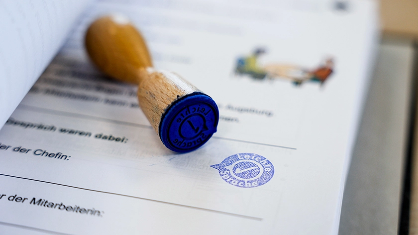 Ein Stempel liegt auf einem Ausdruck. Das Stempelmotiv zeigt das Qualitätssiegel des Netzwerks Leichte Sprache. 