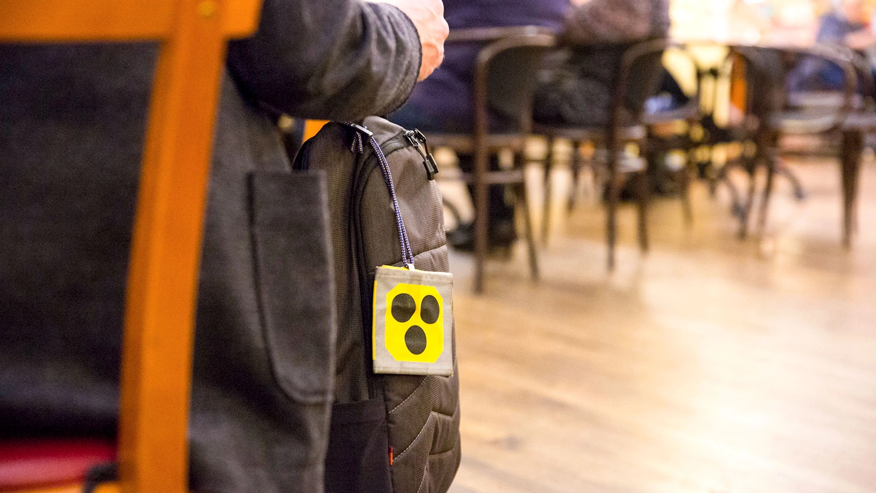 Nahaufnahme: Ein Mann sitzt auf einem Stuhl; an seiner Tasche hängt das Blindenabzeichen.