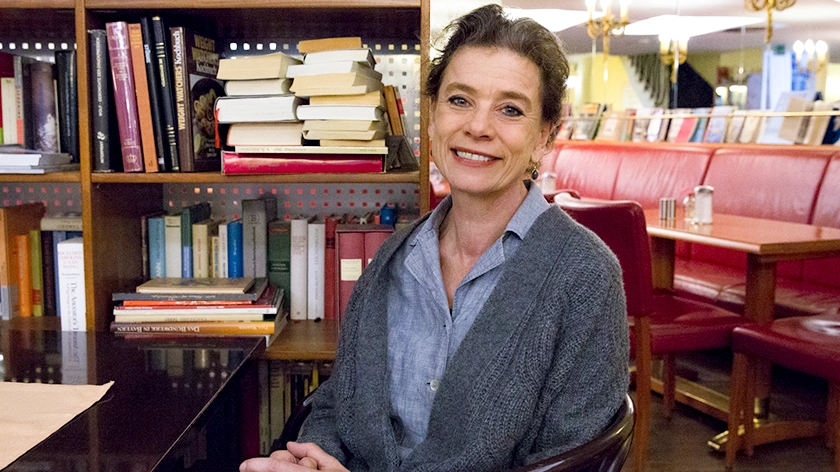 Eine Frau sitzt vor einem Bücherregal und schaut in die Kamera.