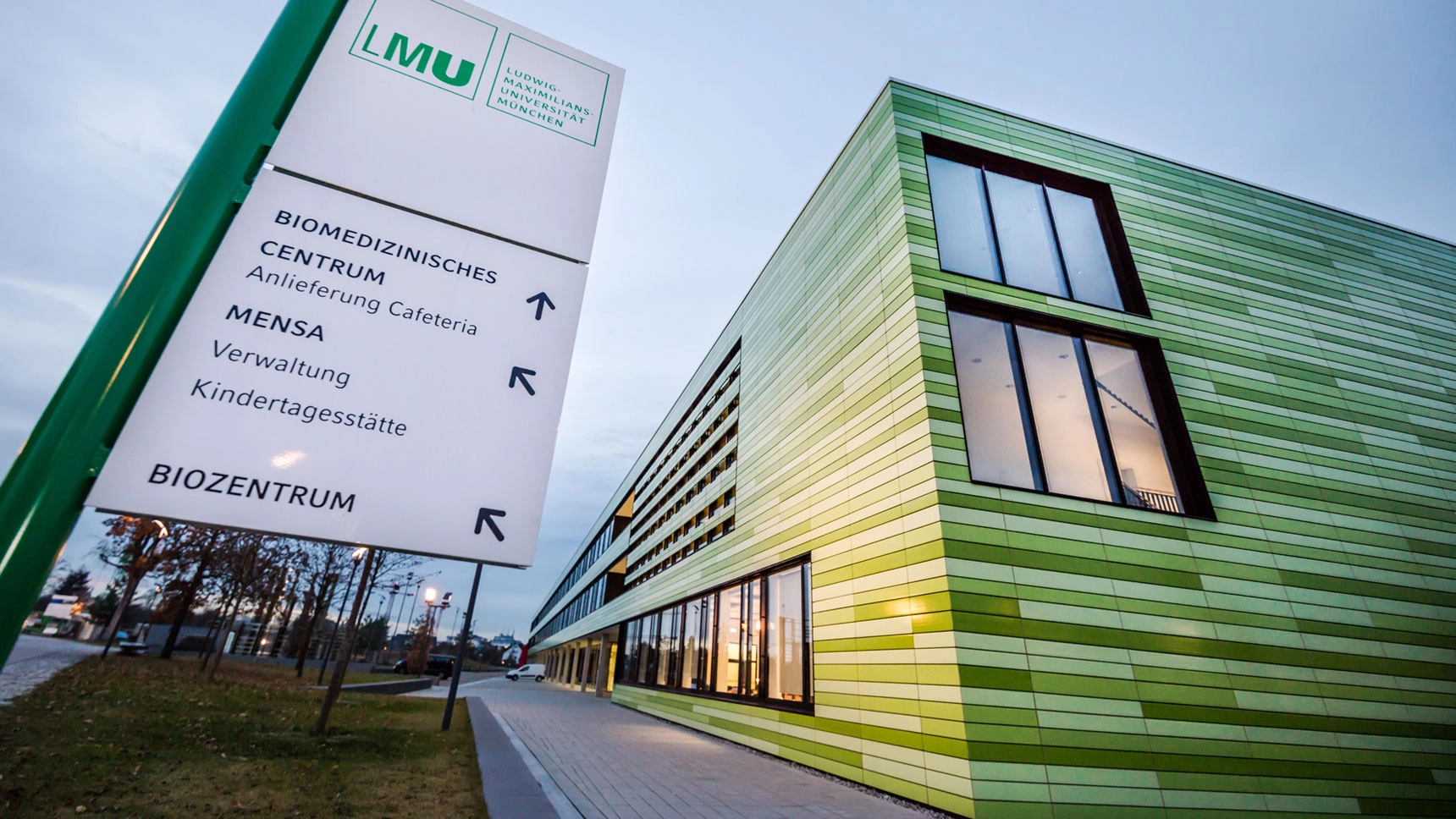 Großer Campus-Wegweiser vor einem modernen Gebäude.